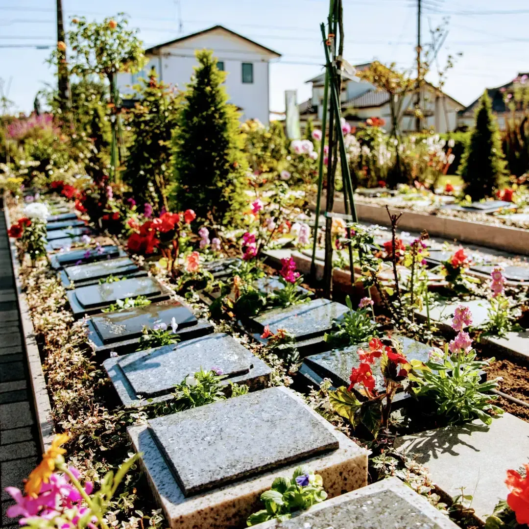 カラフルな花々に囲まれた樹木葬の区画。黒とグレーの墓石プレートが並ぶ穏やかな霊苑の風景。